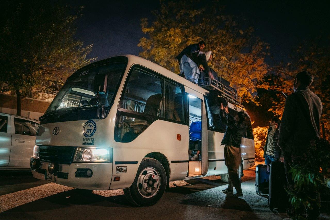 Menschen, die bei Nacht einen Kleinbus beladen und Koffer auf den Dachgepäckträger laden