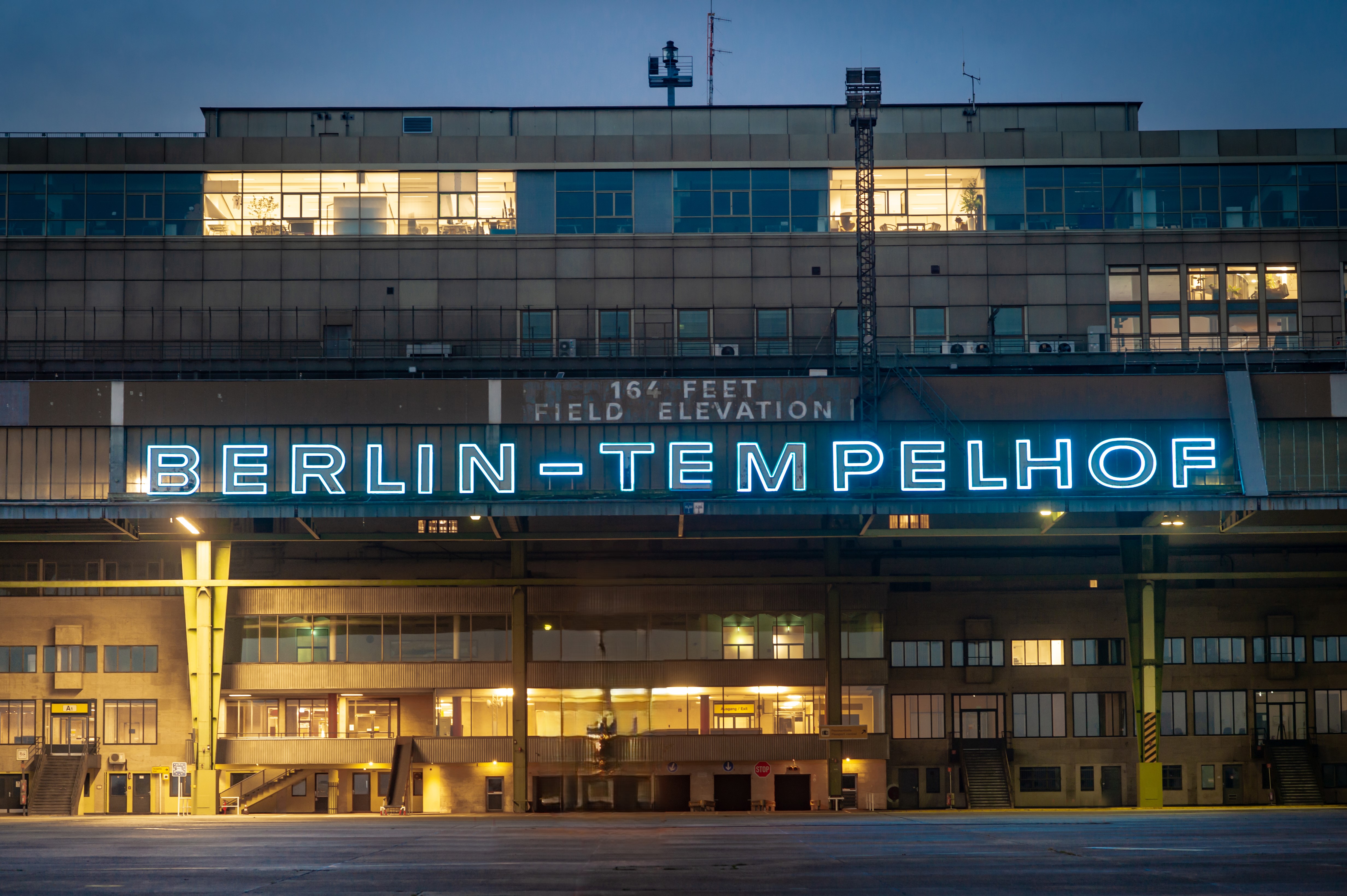 Fassade des Flughafen Tempelhof mit dem Ikonischen Schriftzug "Berlin-Tempelhof", der in der Dämmerung blau leuchtet