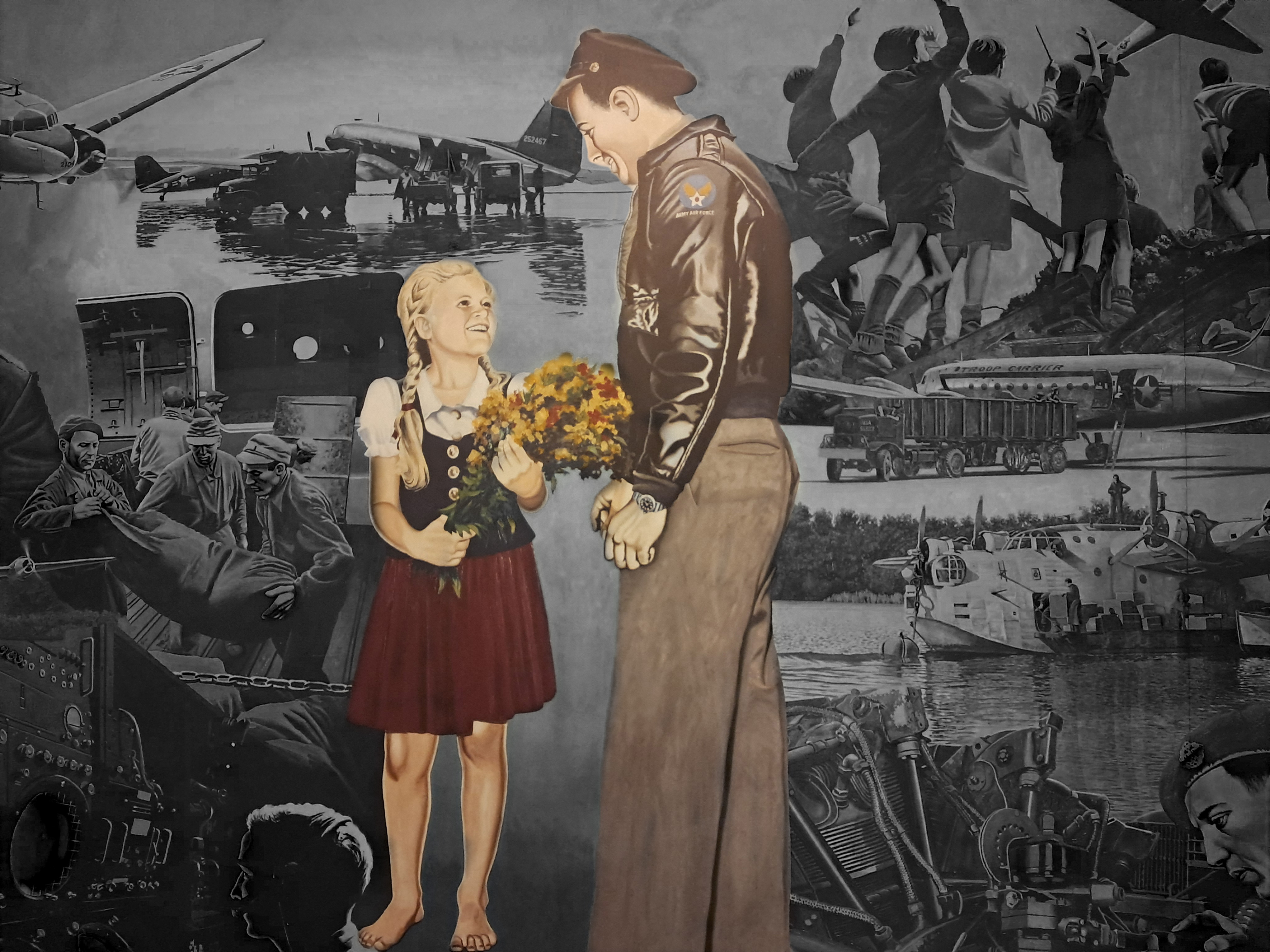 Foto von dem Gemälde in der Haupthalle des Flughafen Tempelhof, auf dem ein Soldat zu einem Mädchen runterschaut, das einen Blumenstrauß in der Hand hält und barfuß ist