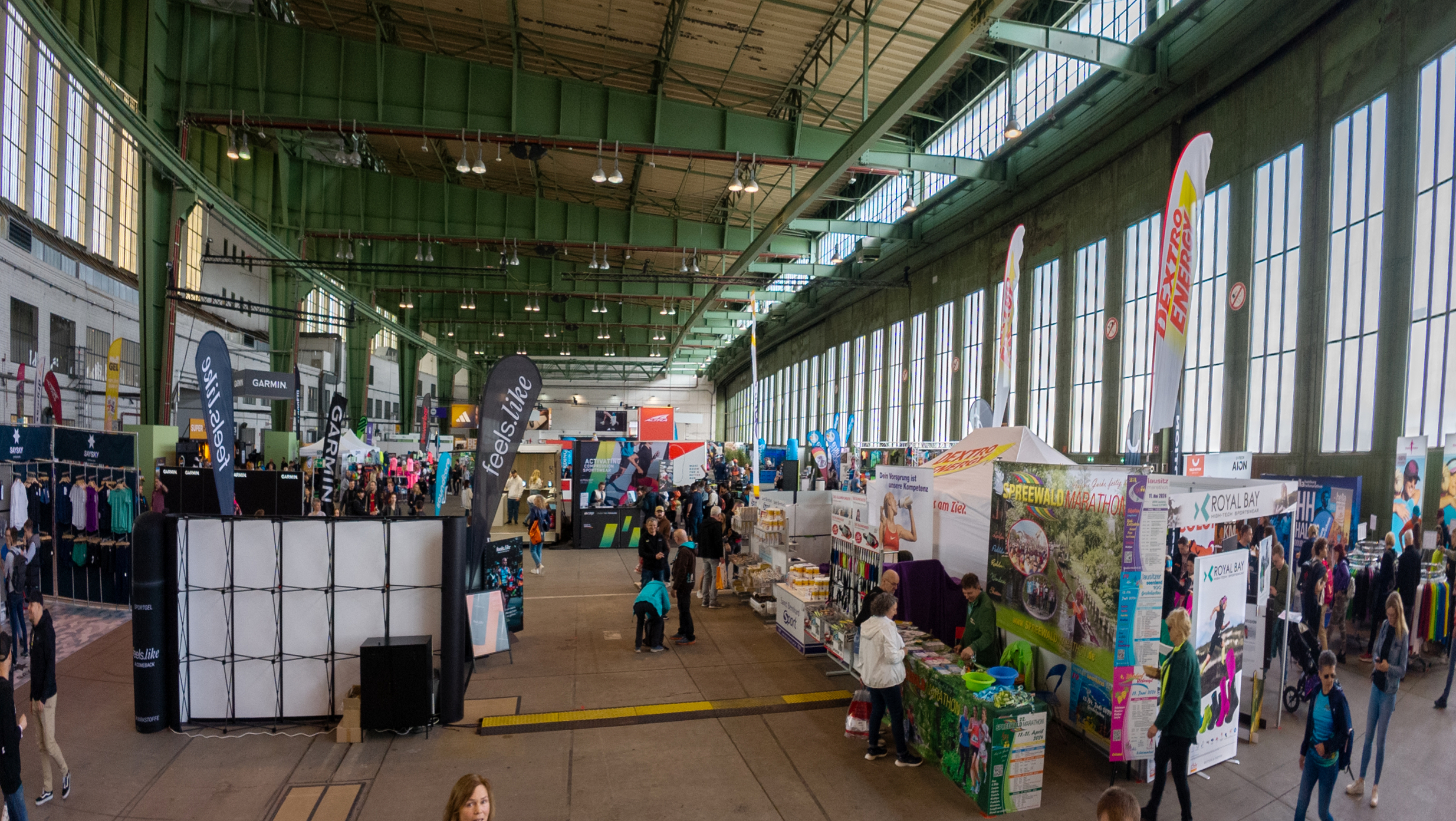 Blick in den Hangar am Flughafen Tempelhof, in dem während der Messe zum Halbmarathon Stände und Flaggen aufgestellt sind. Menschen stehen herum und schauen sich die Stände an