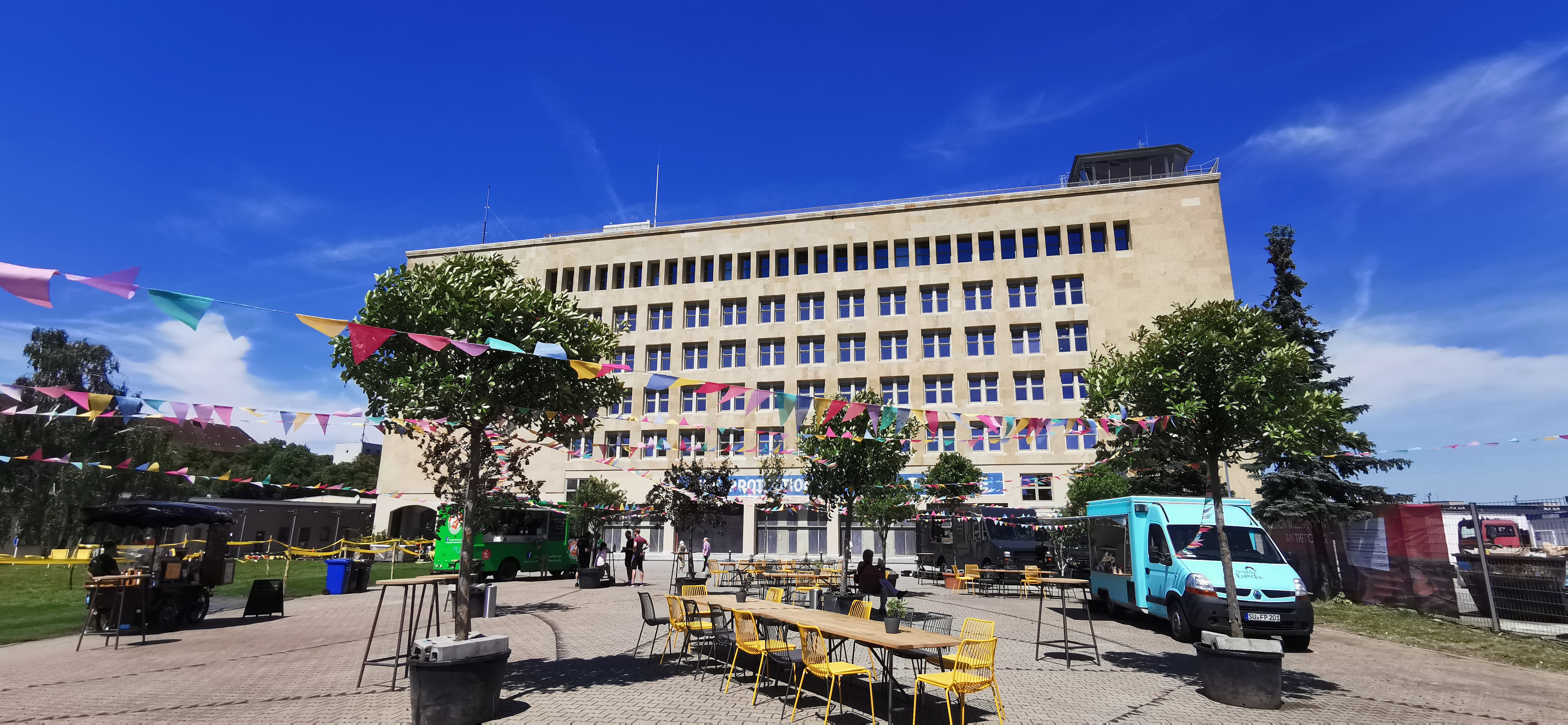 Blick auf die Außenfassade des THF TOWER. Auf der Außenfläche stehen Foodtrucks 